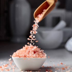 Himalayan pink salt in crystals is poured into a small white bowl.